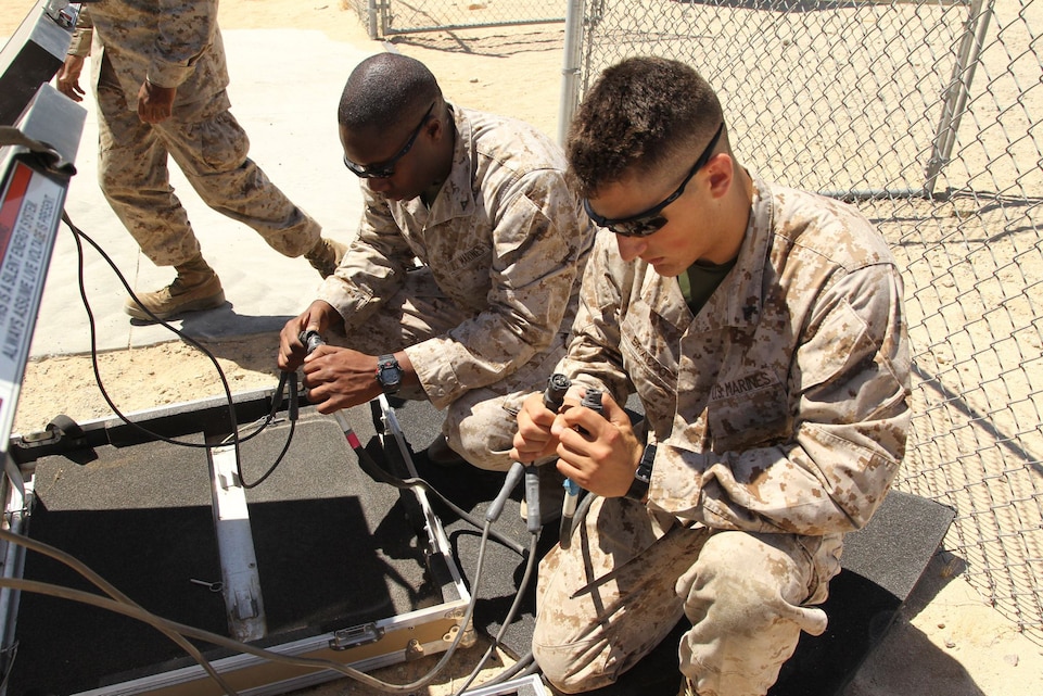 Lance Cpls. Chris Joe and Chris Bracco, data technicians, 6th Communications Battalion, connect solar panel components to the converter of the Ground Renewable Expeditionary Energy Network System during a class at the Western Area Research Test and Evaluation Center 