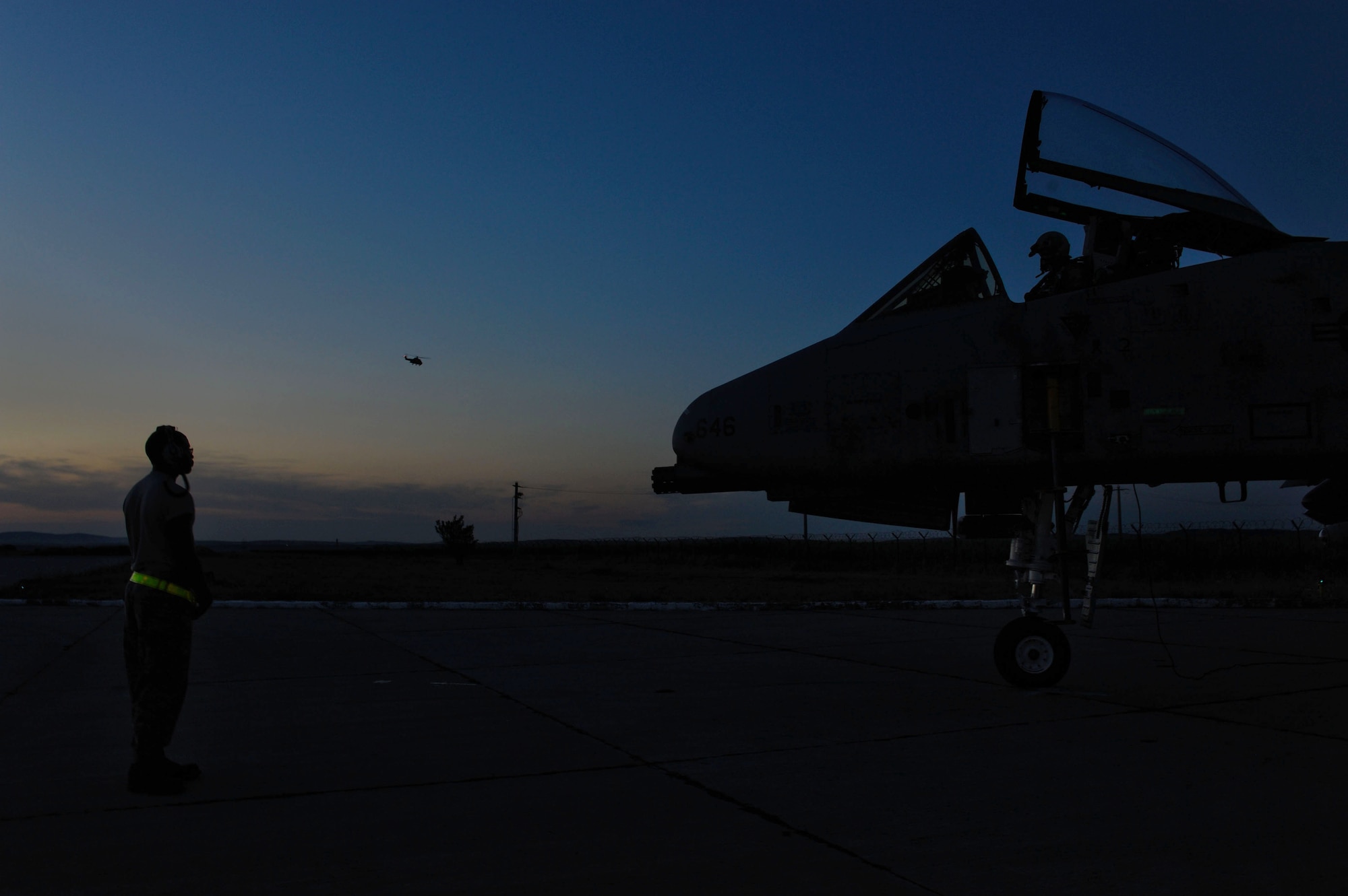 CAMPIA TURZII, Romania – A maintainer with the 81st Fighter Squadron stands ready to marshal an A-10 Thunderbolt II as a Romanian IAR 330 helicopter flies above the flightline here July 20 during Dacian Thunder, a partnership building exercise. Dacian Thunder is a month-long exercise in which U.S. Air Force, Romanian air force, U.S. Marine Corps and the Royal Air Force exchange techniques, tactics, and procedures to strengthen coalition and joint capabilities. (U.S. Air force photo by Senior Airman Natasha Stannard/Released)
