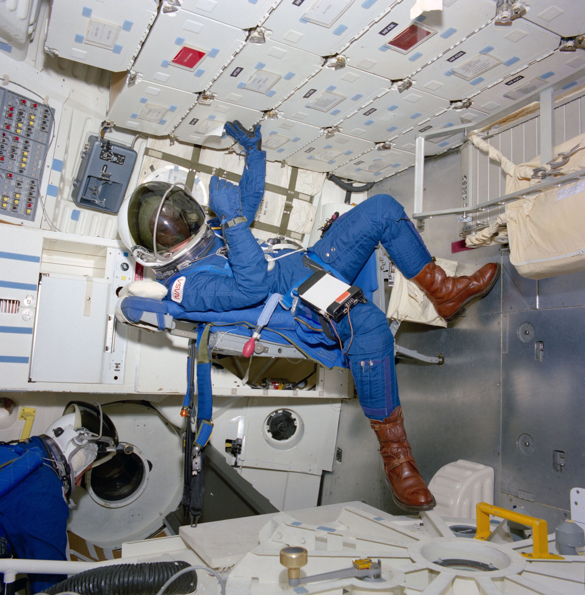 Astronaut George D. Nelson, STS-26 mission specialist, is followed into the mid deck by an unidentified crewmember in the crew compartment trainer (CCT) in the Shuttle Mockup and Integration Laboratory during a March 10, 1988, crew station review. The crew donned new partial pressure suits to evaluate crew equipment and procedures related to emergency egress methods and proposed crew escape options. (NASA photo)