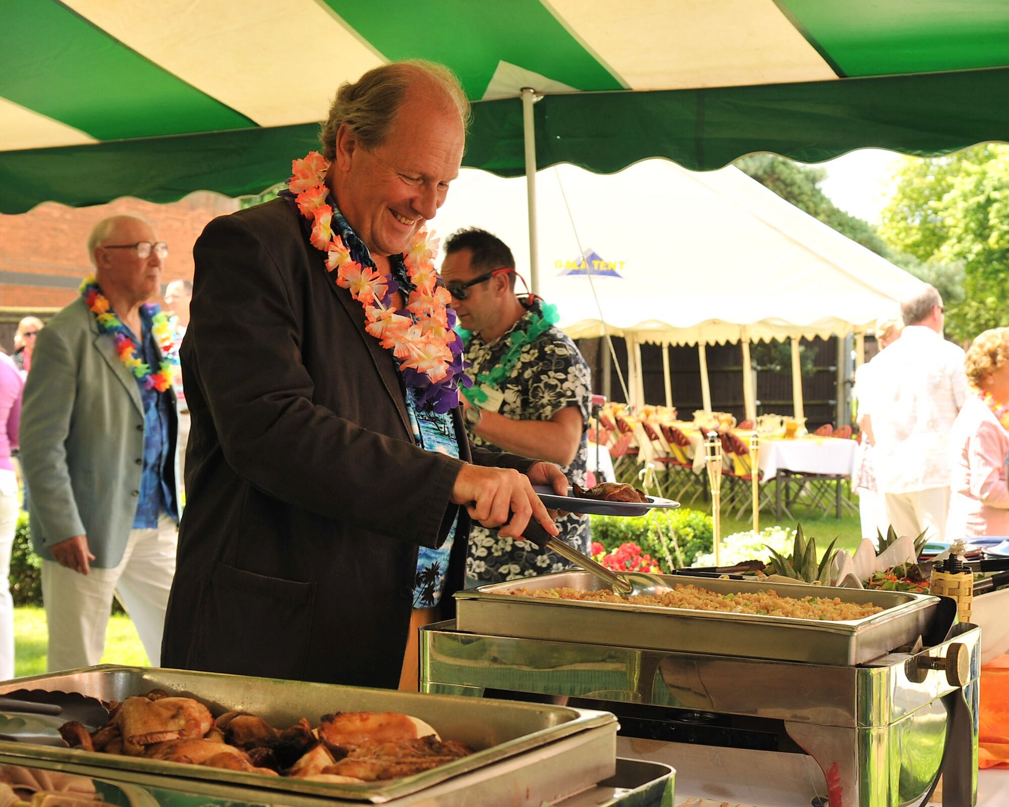 RAF MILDENHALL, England – Charles Holloway, spouse of Georgina Holloway, 100th Air Refueling Wing honorary commander, goes through the buffet line during the New Mayor’s Barbecue held on base July 21, 2012. The Hawaiian luau-themed event featured island-style cuisine including fried rice, coconut shrimp and a roast pig. (U.S. Air Force photo/Senior Airman Jerilyn Quintanilla)