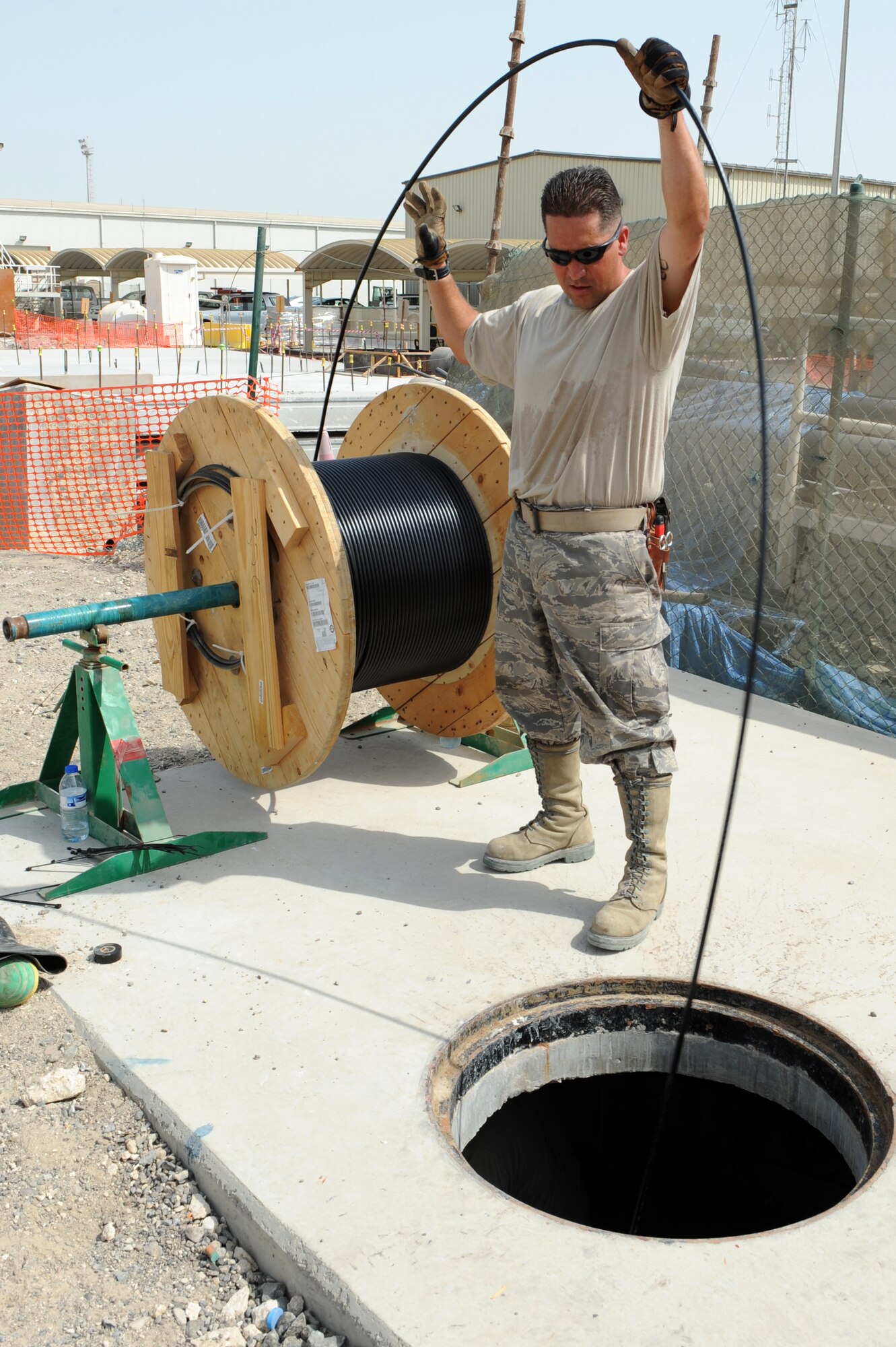 SOUTHWEST ASIA - U. S. Air Force Tech. Sgt. Hans Pugh, 380th Expeditionary Communications Squadron cable antenna systems NCO in charge, feeds cable into a manhole at a new construction site July 23, 2012. Pugh, an Austin, Texas native, is deployed to the 380th Air Expeditionary Wing from Kadena Air Base, Japan. (U.S. Air Force photo/Master Sgt. Scott MacKay)