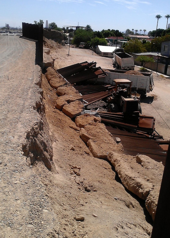 ANDRADE, Calif. (July 25, 2012) – A 120-foot section of border fence that fell over following illegal excavation on the Mexican side of the border July 24 sits atop construction equipment used in the digging. The U.S. Army Corps of Engineers Los Angeles District, working with U.S. Customs and Border Protection agents, are working to secure the area and replace the damaged section. (USACE photo)