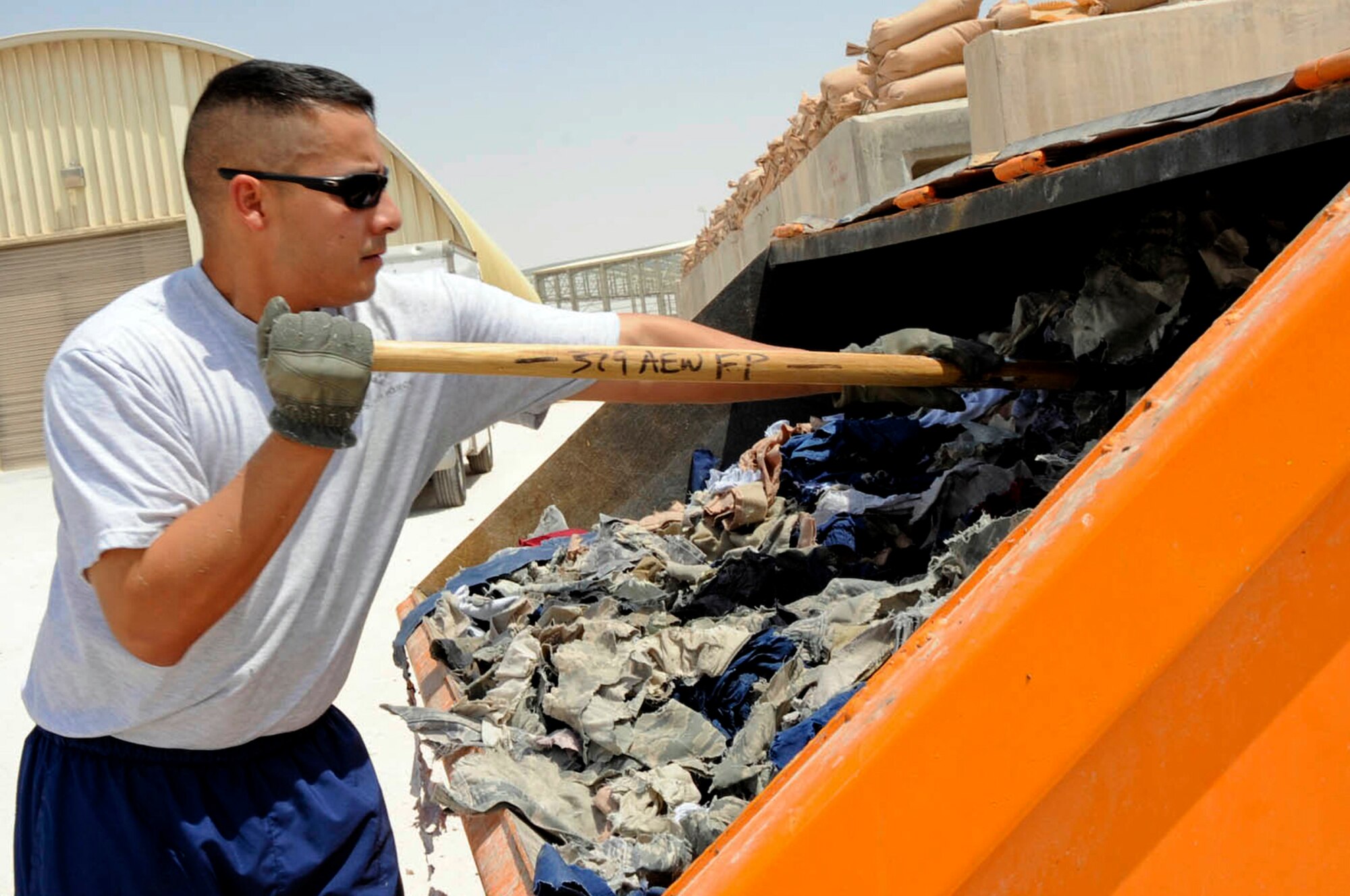 U.S. Air Force Tech. Sgt. Michael Benitez, 379th Air Expeditionary Wing Force Protection, pushes shredded uniform items into the dumpster, Southwest Asia, July 24, 2012. Benitez, deployed from Schriever Air Force Base, Colo.,  a native of San Bernardino, Calif., supports the 379th Air Expeditionary Wing OPSEC program with his efforts.  (U.S. Air Force photo/Staff Sgt. Sheila deVera)