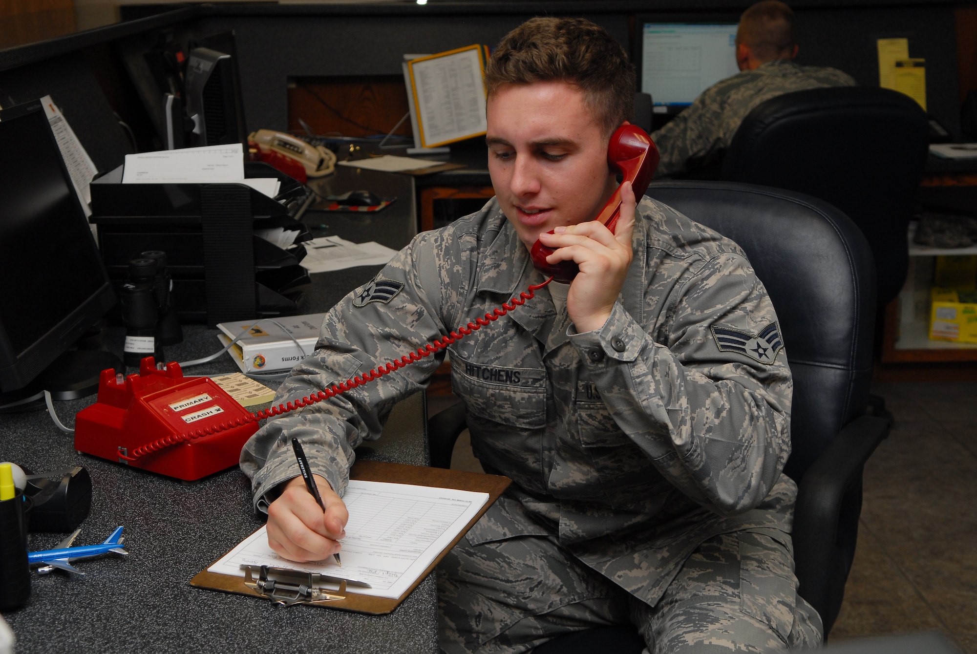 Senior Airman Kory Hitchens, 56th Operations Support Squadron Airfield Management Operations shift lead, picks up the primary crash phone July 25 at the Luke Air Force Base operations building. The phone rings whenever there is an in-flight or ground emergency. (U.S. Air Force photo by Airman 1st Class Grace Lee)