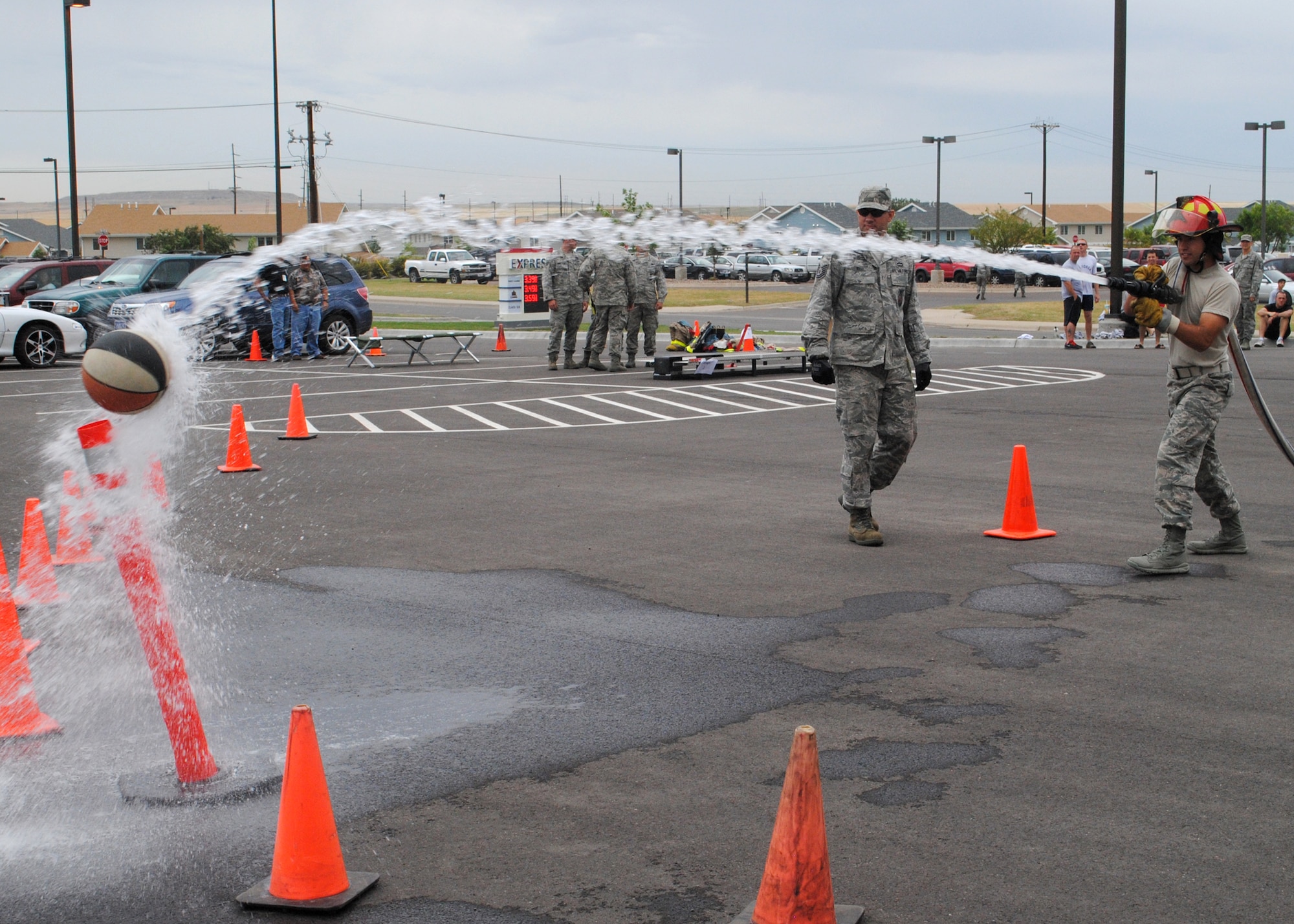2nd Lt. Christopher Foti, 341st Security Forces Squadron flight commander, uses a fire hose to knock a basketball off of a cone as Tech. Sgt. Jeremy Wray, 341st Civil Engineer Squadron firefighter, waits to take the hose before he moves to the Bucket Brigade.  Wray along with other members of Malmstrom’s fire department were at the Fire Muster competition cheering on other members participating.  (U.S. Air Force photo/Airman 1st Class Cortney Paxton)