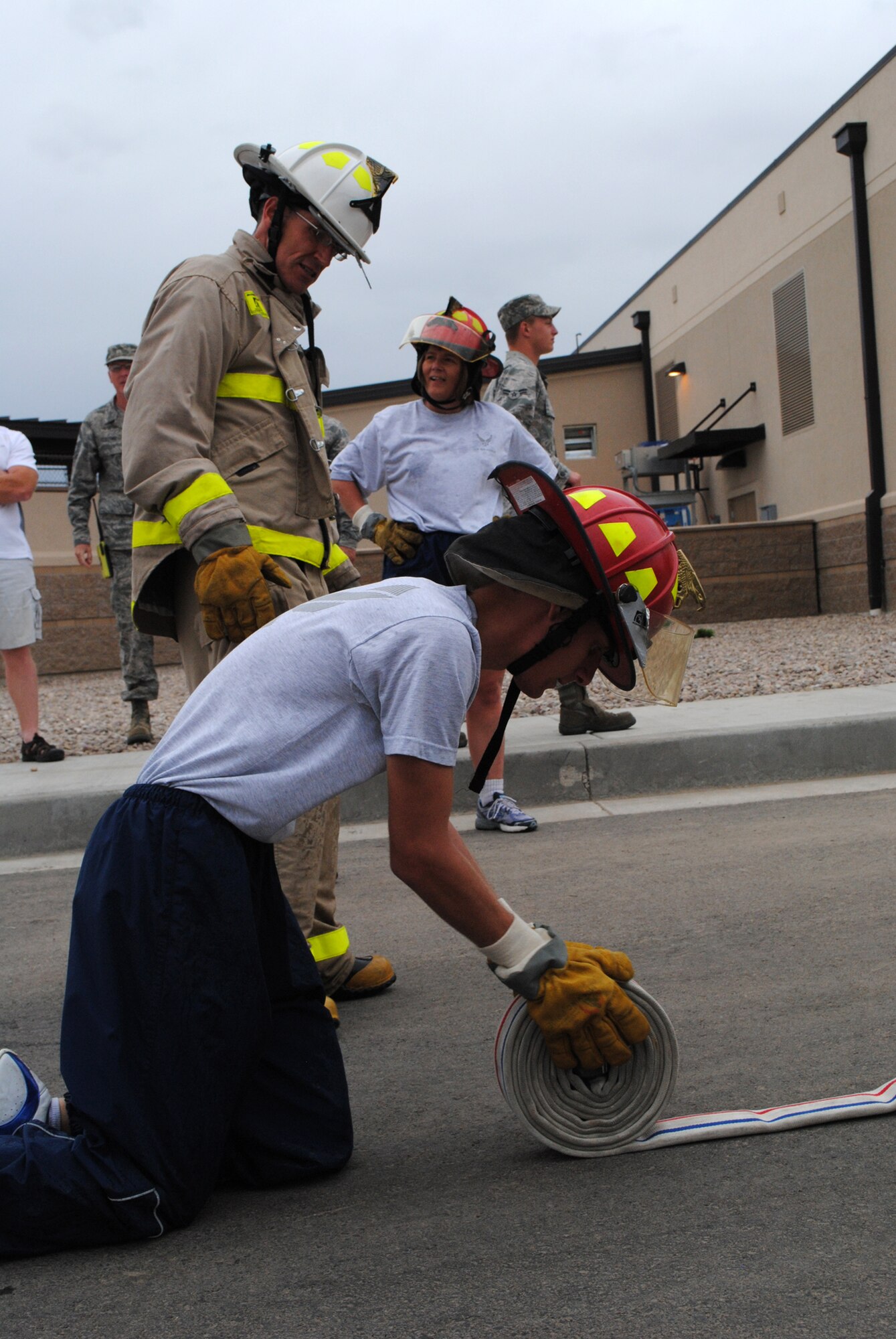 Senior Airman Terry Butterfield, 341st Mission Support Group knowledge operator, rolls a fire hose as his teammates Chief Master Sgt. Duane Buchi, 341st MSG superintendant, and Col. Angela Stout, 341st MSG commander, cheer him on.  Rolling a hose was one of seven stations in the Fire Muster Competition. 