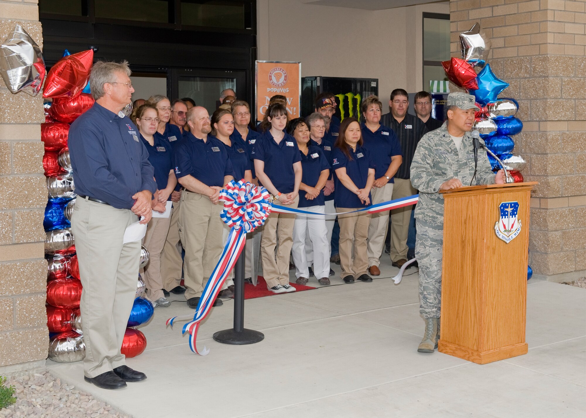 Col. H.B. Brual, 341st Missile Wing commander, addresses the audience prior to the official ribbon cutting opening the new Exchange store on July 20. Mark Downs, (left) store manager and all of the other Exchange employees are pictured in the background. (U.S. Air Force photo/Beau Wade)
