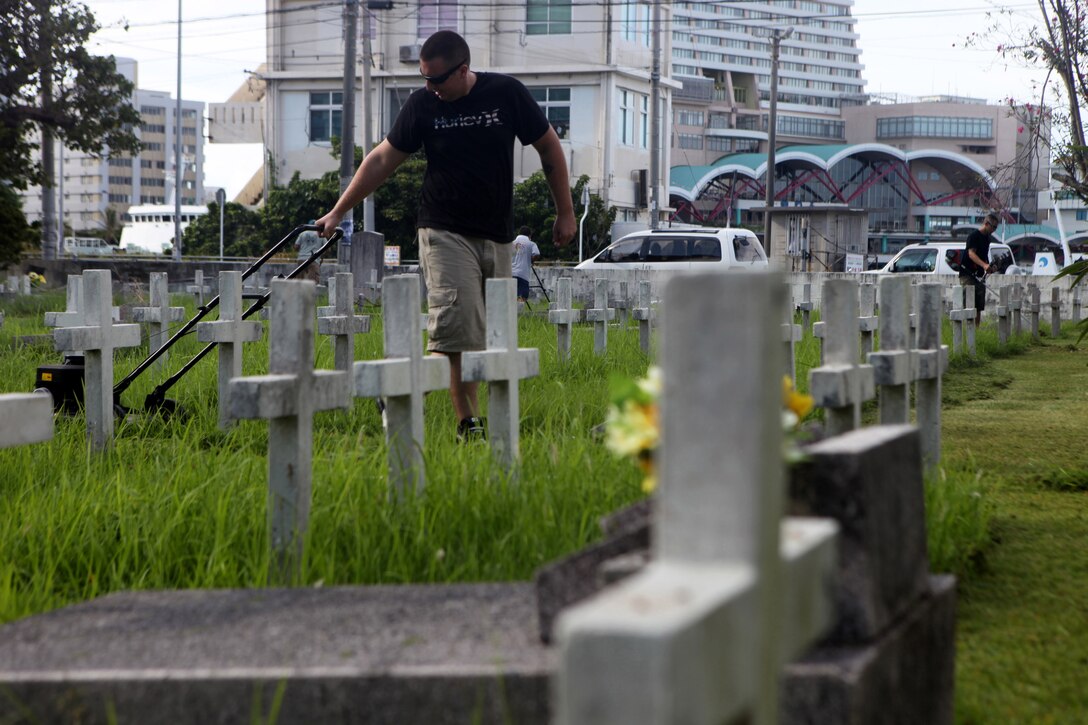 NAHA, Okinawa, Japan - An Airmen from the 18th Air Wing based at Kadena Air Force Base, mows grass at the Tomari International Cemetery here, July 29. Through the efforts of one young Boy Scout, Gabriel Vasquez, military members from nearly every branch of service came together to revitalize a local cemetery where numerous veterans are buried.