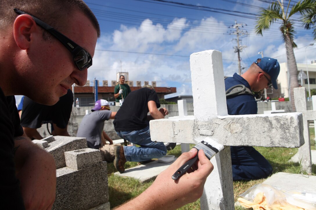 NAHA, Okinawa, Japan -- Military members from the Marine Corps, Navy and Air Force join civilian volunteers to paint veterans’ crosses at the Tomari International Cemetery here, July 29. Through the efforts of one young Boy Scout, Gabriel Vasquez, military members from nearly every branch of service came together to revitalize a local cemetery where numerous veterans are buried.