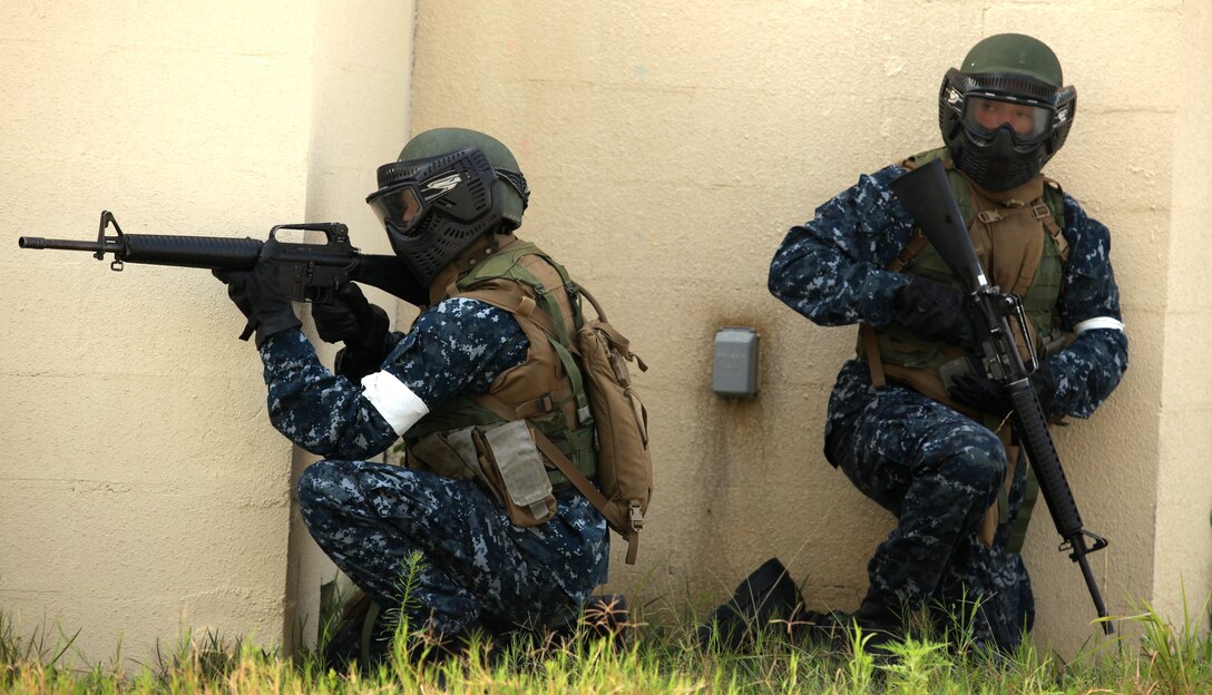 Two midshipmen hide behind cover while they scan the simulated battlefield for enemies while practicing Military Operations on Urban Terrain aboard Marine Corps Base Camp Lejeune July 25. Midshipmen found MOUT was easier to do if they used each other and worked as a team, instead of trying to survive by themselves.