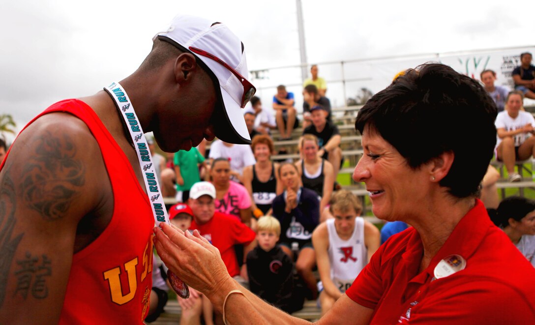 Beckie Page, assistant manager of the Semper Fit Center, Marine Corps Base Hawaii, presents a medal to Staff Sgt. Thomas Gouard, substance abuse control officer for Combat Logistics Battalion 3, 3rd Marine Logistics Group, during an award ceremony following the annual Camp Smith 5K Grueler here, July 28. Gouard, 30, from Danville, Ill., finished the 3.1-mile race in 20:24, negotiating multiple hills and challenging rainforest terrain to finish with the best time among all Marine competitors. “I heard about how hilly it was, and the trails, that’s why I wanted to run the race,” said Gouard. “It’s a pretty good course, and I definitely plan to come out again next year.”