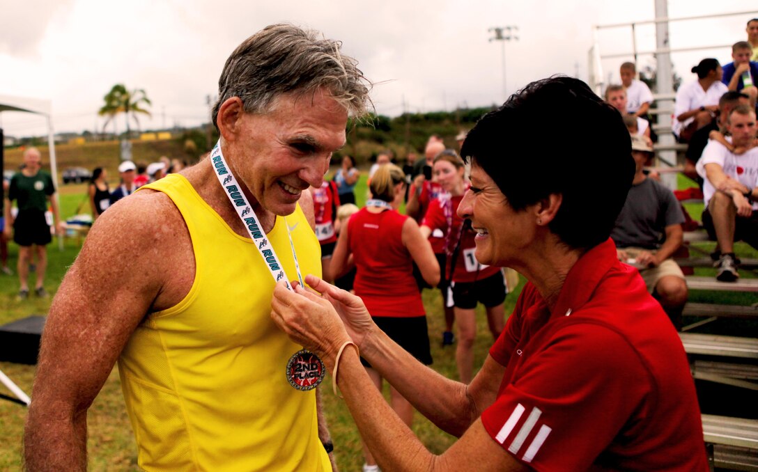 Beckie Page, assistant manager of the Semper Fit Center, Marine Corps Base Hawaii, presents a medal to Jim Murray, a 60-year-old resident from Honolulu, during an award ceremony following the annual Camp Smith 5K Grueler here, July 28. “Sometimes I wonder what I’m doing out here,” joked Murray, who works as the public affairs officer for the Fleet Logistics Center at Joint Base Pearl Harbor-Hickam. Murray has competed in nearly 20 similar races at Camp H.M. Smith during his 30 years on the island.
