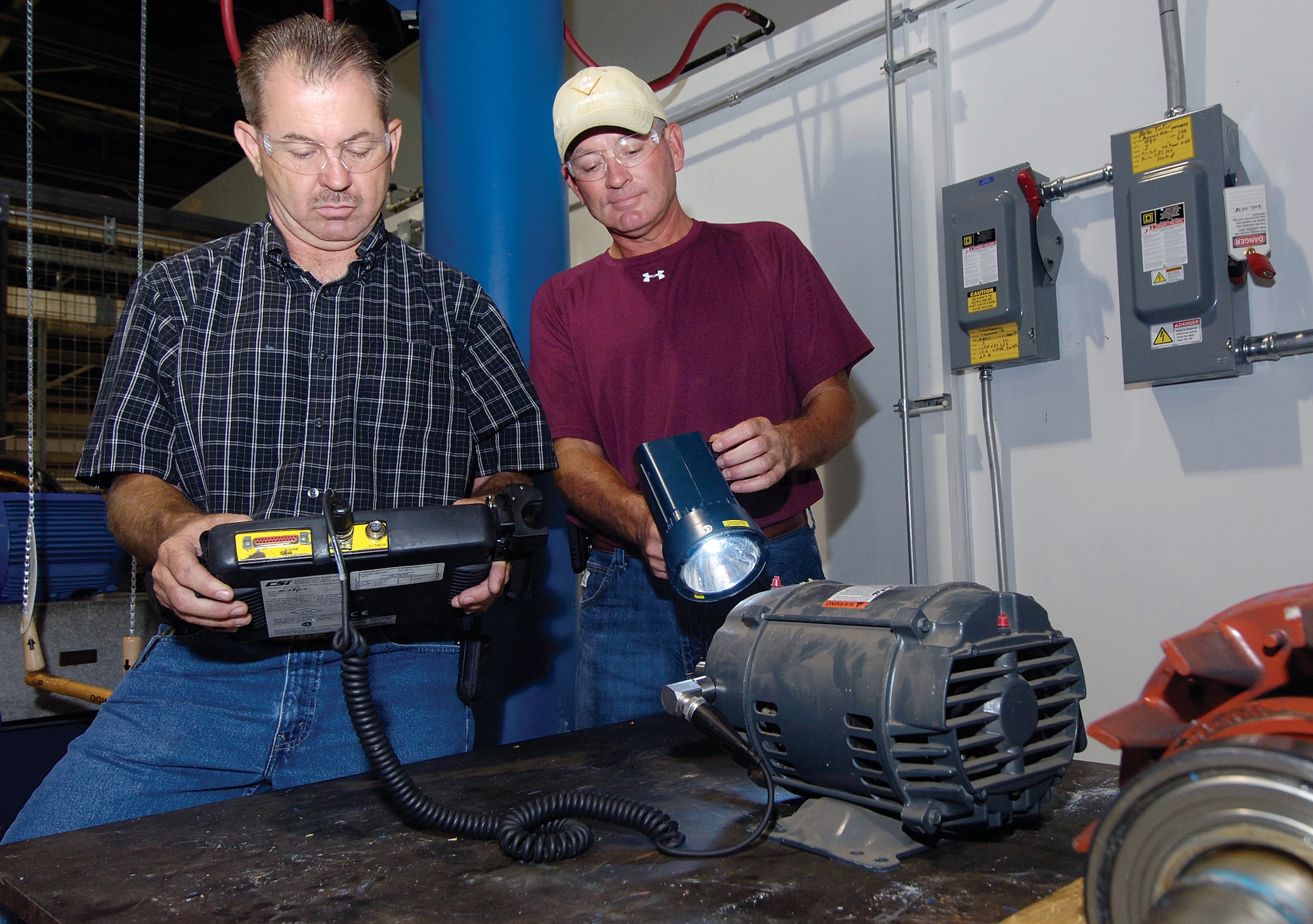 Engineering technicians Danny McClure, left, and Eric Buchanan, members of the 76th Maintenance Group Predictive Maintenance Team, will perform vibration checks on all sizes of industrial shop motors, working to prevent the breakdown of equipment which slows production. Fractional horsepower to 3,000 horsepower motors are inspected to ensure they meet standards.  The handheld machine of Mr. McClure checks for vibration problems and Mr. Bucahanan syncs a strobe light with the rotating fan which visually slows the motion allowing him to see the fan and belts operate. 