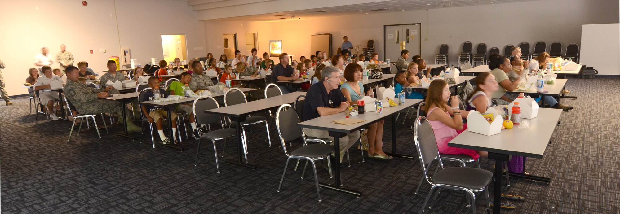 Kids and their parents watch a movie and eat lunch to finish off the annual Bring Your Kids to Work Day at Dobbins Air Reserve Base, July 27. Members of Dobbins ARB were able to bring their kids to their places of work, then to a hangar with several hands-on displays of equipment utilized on the base and also to the C-130 flight simulator. (U.S. Air Force photo/Brad Fallin)