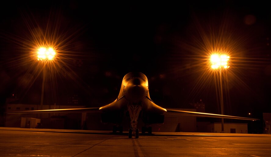 A B-1 bomber shrouded in the glow of lights in the aircraft parking area sits silently at Ellsworth Air Force Base, S.D., July 24, 2012. The B-1 is a long-range, multi-role heavy bomber that can reach speeds of 900-plus miles per hour. (U.S. Air Force photo by Airman 1st Class Zachary Hada/Released)