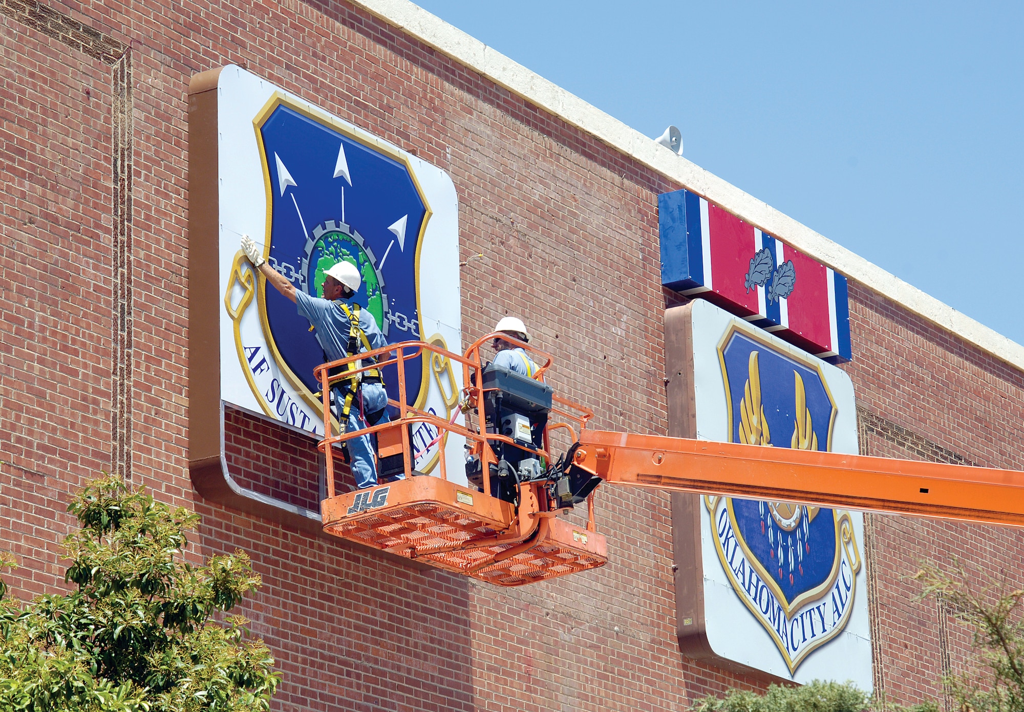 The transformation continues to the face of Bldg. 3001 with the addition of the new Air Force Sustainment Center shield installed July 20. The 72nd Air Base Wing Civil Engineering Directorate’s Eddie Boyd, left, and Gregg Garrison shrug off a triple-digit summer day and install the new sign in three sections. (Air Force photo by Margo Wright)