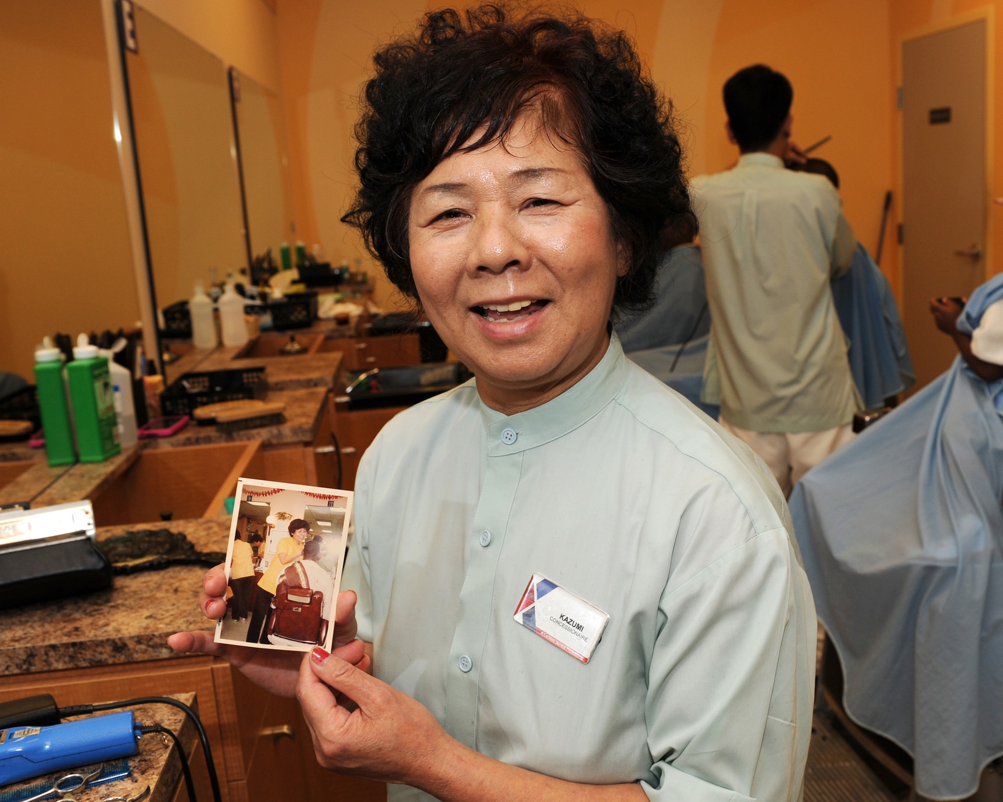 Kazumi Oshiro, Army & Air Force Exchange Service barbershop manager, looks at an old photo taken more than 40 years ago, trimming the hair of a customer on Kadena Air Base, Japan, July 18, 2012. Oshiro has been working at the base barber shop since 1965 and has given an estimated 497,495 haircuts during her 47-year career. (U.S. Air Force photo/Junko Kinjo)