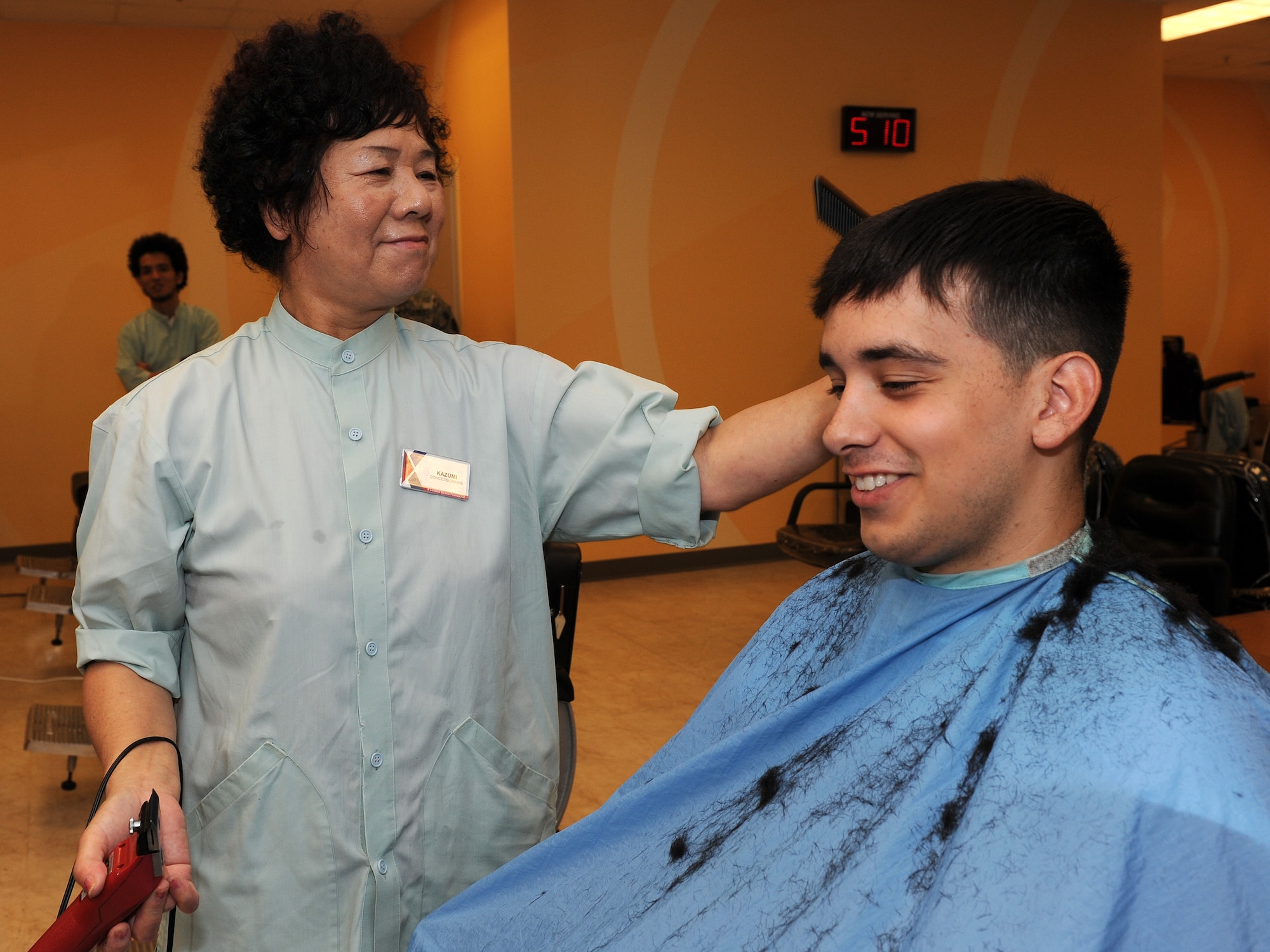 Kazumi Oshiro, Army & Air Force Exchange Service barber shop manager, trims the hair of Airman 1st Class Richard Tato, 18th Component Maintenance Squadron, aerospace propulsions technician, on Kadena Air Base, Japan, July 18, 2012. Oshiro has been working at the base barber shop since 1965 and has trimmed an average of 200 customers per week, or 10,585 customers per year. (U.S. Air Force photo/Junko Kinjo)