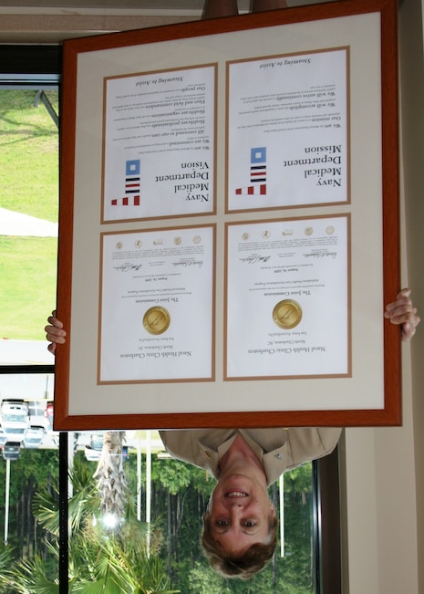 Naval Naval Health Clinic Charleston Commanding Officer, Capt. Mary Kim Kenney-Gutshall announces the inspection dates of an upcoming Joint Commission inspection to the staff of NHCC at Joint Base Charleston - Weapons Station, S.C.,  while displaying the accreditation seals awarded by the Joint Commission following their previous visit. (U.S. Navy photo/Jeff Kelly)
