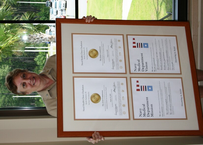 Naval Naval Health Clinic Charleston Commanding Officer, Capt. Mary Kim Kenney-Gutshall announces the inspection dates of an upcoming Joint Commission inspection to the staff of NHCC at Joint Base Charleston - Weapons Station, S.C.,  while displaying the accreditation seals awarded by the Joint Commission following their previous visit. (U.S. Navy photo/Jeff Kelly)