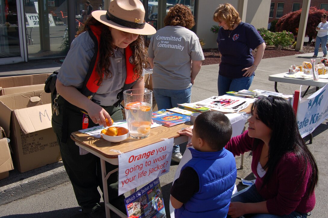 These photos are from Cherry Fest which was April 28th, 2012.  Ranger Amber Tilton partnered with the local Columbia Gorge Safe Kids organization and joined them at their booth to educate the community about safe practices around water.

Notice the sign: "Orange you going to wear your life jacket?"  By peeling a tangerine and dropping it in water, it will sink. However, with the peel on, it floats. This provides a good way to talk about wearing a Personal Flotation Device. By peeling an orange and then holding it around the orange and dropping it in, you can talk about making sure your jacket is the right size, otherwise it may not work (as demonstrated when the peel floats to top and the orange sinks). 

Also notice that Ranger Tilton is wearing an inflatable PFD. She gets a lot of comments on this, because people (men especially) do not realize that inflatables are an option.  

Safe Kids handed out free bike helmets that day and educated people about car seat safety.