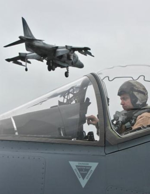 An AV-8B Harrier hovers above the flight deck of the USS Peleliu and a second Harrier pilot during daily flight operations as part of PHIBRON Three and 15th MEU’s PHIBRON-MEU Interoperability Training off the coast of southern California, June 1. The purpose of the exercise is to give Marines and sailors the opportunity to become familiar working together as a blue-green team, a must when it comes to flight deck operations.::r::::n::::r::::n::::r::::n::