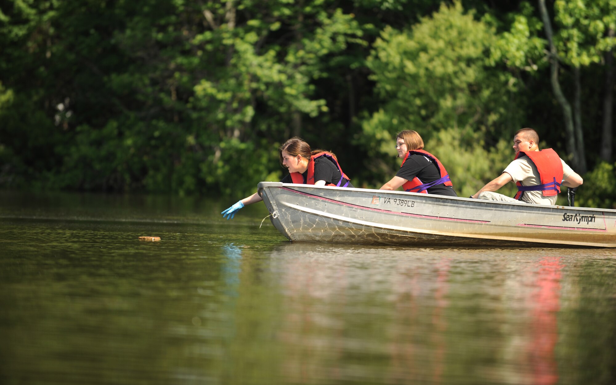 Airman 1st Class Mallorie Poole, left, 1st maintenance Squadron line delivery technician, reaches for a piece of trash floating on the Chesapeake Bay, Va., June 2, 2012. Poole, and the other Airmen in her boat, came together for the 2012 Clean the Bay Day event at Langley Air Force Base. (U.S. Air Force photo by Senior Airman Jarad A. Denton/Released)