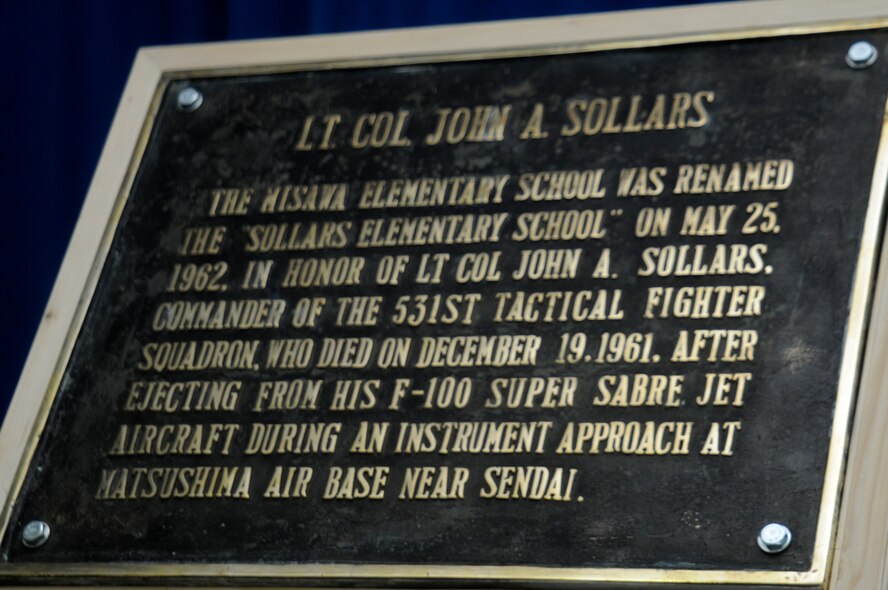 A plaque shares the heroic story of Lt. Col. John A. Sollars at the 50th Anniversary of Sollars Elementary School dedication ceremony at Misawa Air Base, Japan, June 1, 2012. The plaque was originally made for the school in 1962, but was lost when the school was rebuilt in 1998.  It had been missing for over 10 years, but was found and rededicated to the school at the ceremony. (U.S. Air Force photo by Airman 1st Class Zachary Kee/ Released)
