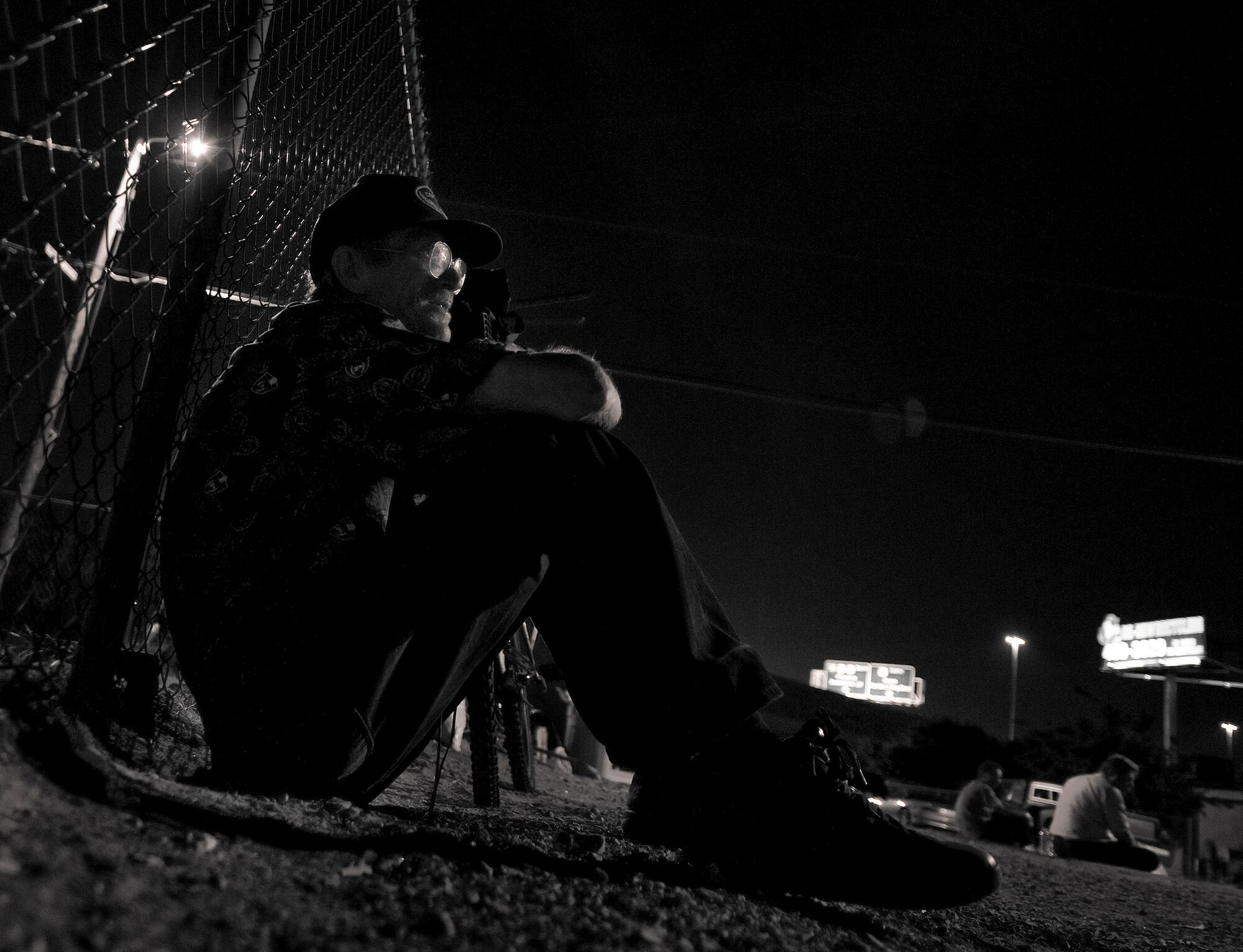A local man sits against a fence and watches as 99th Logistics Readiness Squadron Airmen hand out food to the local community during a monthly Top-3 Food Drive for the Homeless event Apr. 30, 2012, in Las Vegas. The recurring event was established to give back to the community. (U.S. Air Force photo by Airman 1st Class Daniel Hughes)