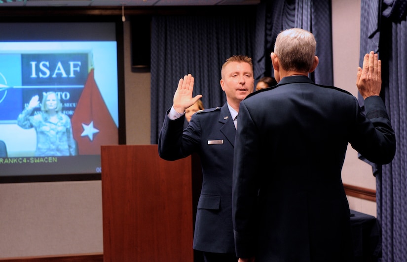 Air Force Chief of Staff Gen. Norton Schwartz administers the oath of office to Maj. Lori Hodge and her husband, Maj. Christian Hodge, during a unique promotion ceremony at the Pentagon in Washington, D.C., June 4, 2012.  Christian attended the ceremony in person while Lori, who is deployed to Kabul, Afghanistan, attended via video teleconference.  The two were promoted from captain to the rank of major during the ceremony.  (U.S. Air Force photo/Andy Morataya)