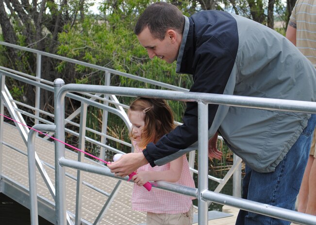 Capt. Gary Myrick, 341st Operations Support Squadron member, shows his daughter Ava, 3, how to hold her fishing pole. The National Kid's Fishing Day event on Malmstrom was open to children of all ages and prizes were available to children ages 3 to 15. (U.S. Air Force photo/Airman 1st Class Cortney Paxton)
