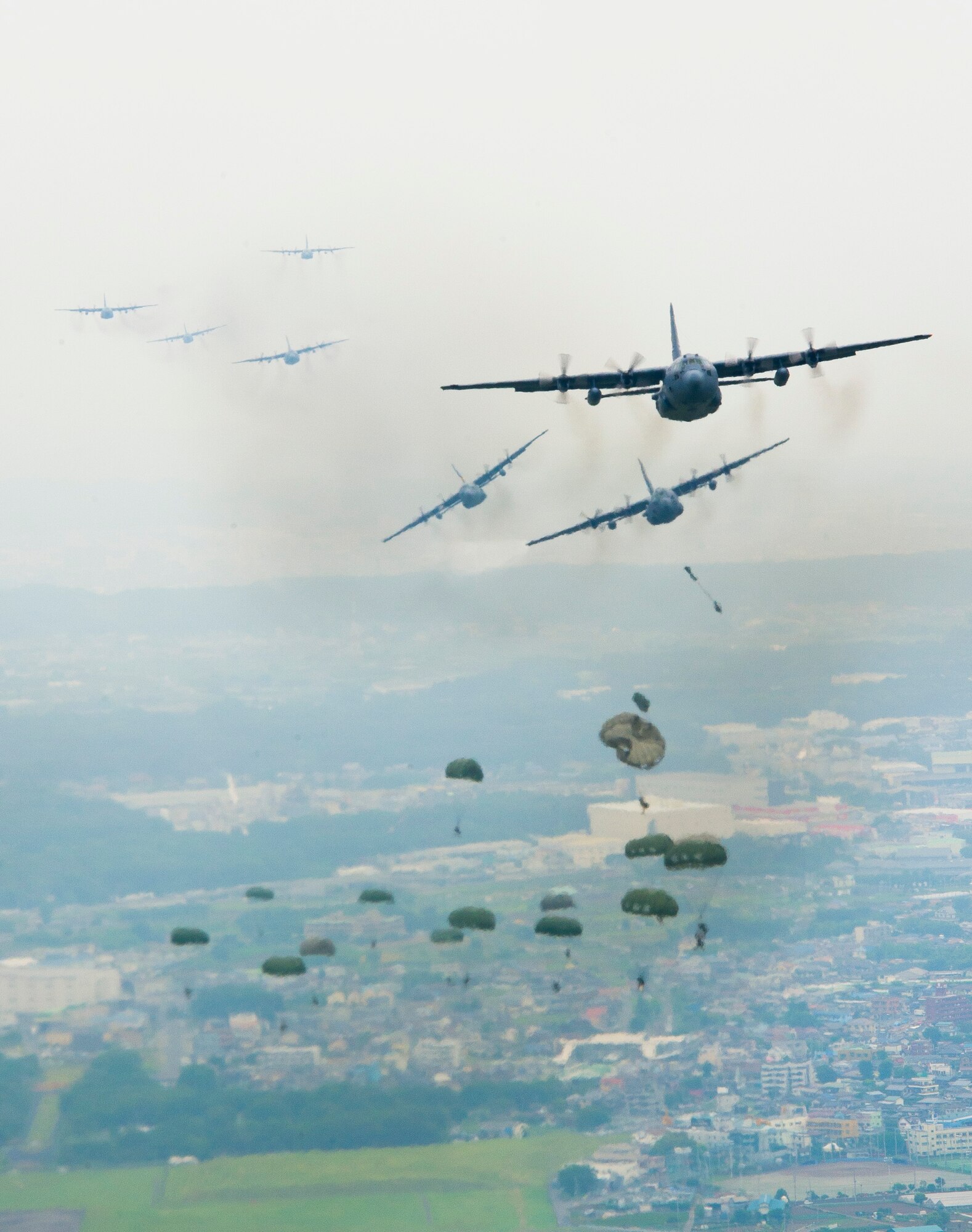 YOKOTA AIR BASE, Japan -- A formation of C-130 Hercules cargo aircraft fly in formation as Army personnel parachute over Yokota Air Base, Japan, on June 5, 2012. Aircrew from the 36th Airlift Squadron participated in the Samurai Surge, an all-day training exercise, testing mission capability of many agencies throughout the base. (U.S. Air Force photo by Staff Sgt. Chad C. Strohmeyer)