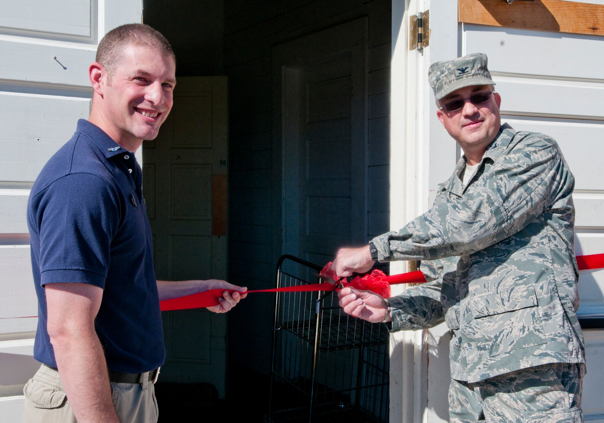 Col. Timothy Dodge, 90th Mission Support Group commander, cuts the ceremonial ribbon, held by Tech. Sgt. Josh Hinsey, 90th Force Support Squadron First Term Airman Center NCOIC and Air Force Sergeants Association Cowboy Chapter 1178 president, commemorating the grand re-opening of the Airman’s Attic in its new location in Building 315 June 2. (U.S. Air Force photo by Airman Jason Wiese)