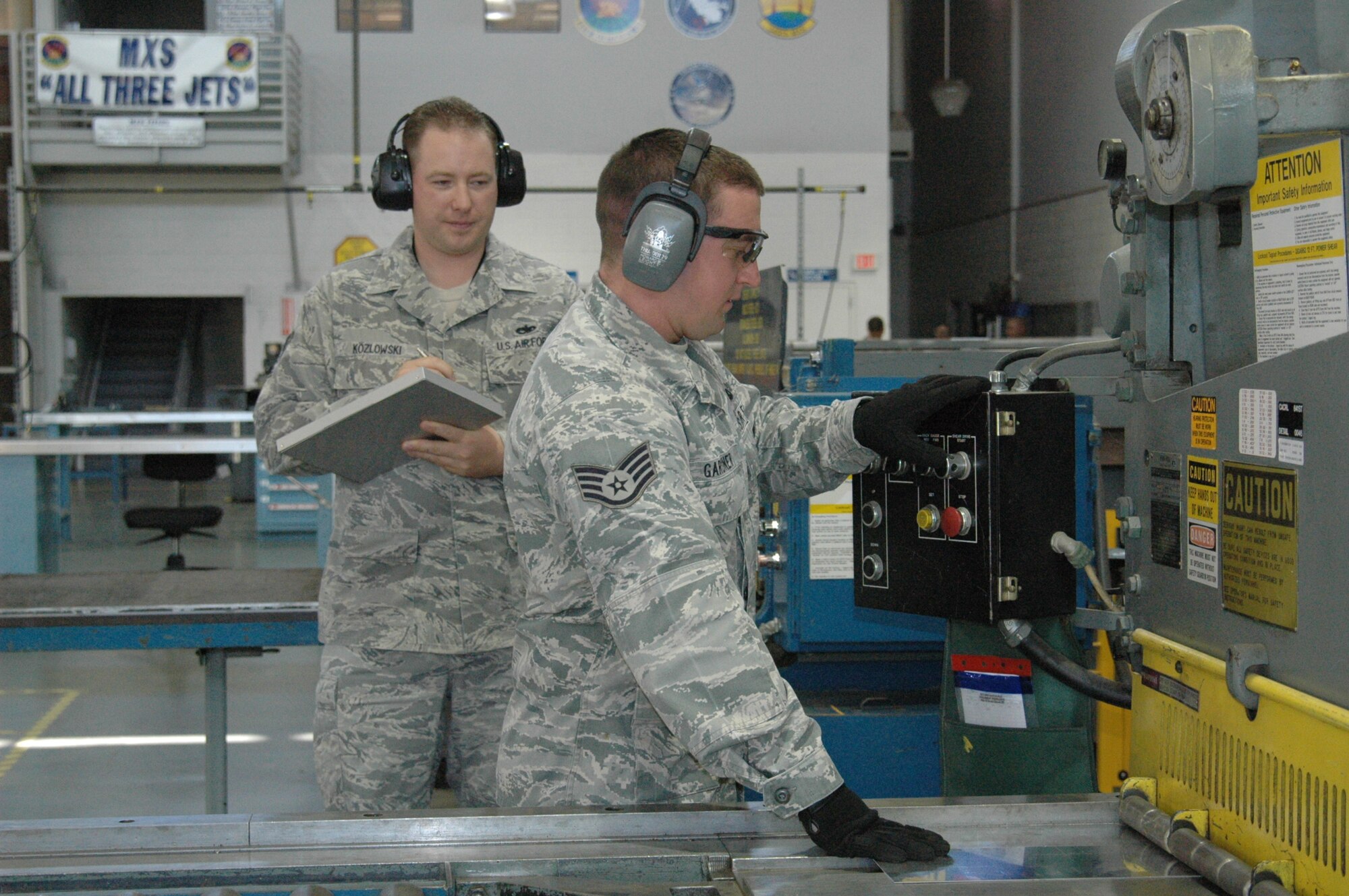 Tech. Sgt. Cory Kozlowski, 60th Maintenance Group environmental, safety and occupational health manager, observes Staff Sgt. Cody Gardner, 60th Maintenance Squadron aircraft structural maintainer, cut sheet metal May 31 in the sheet metal shop. (U.S. Air Force photo/ Tyler Grimes)