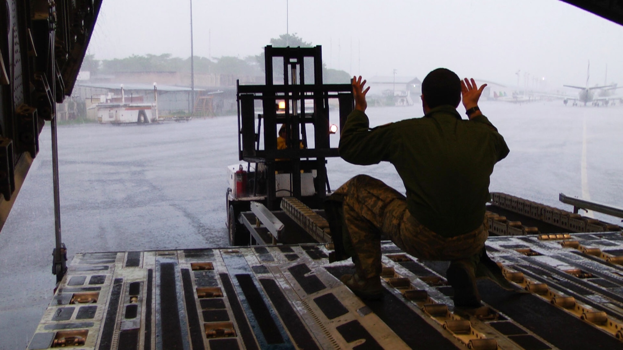 Staff Sgt. Alex Hull directs a forklift driver while offloading humanitarian cargo in Managua, Nicaragua June 9. The 315th Airlift Wing performed a three-day mission while battleing rain to deliver 60,000 lbs of food, clothes, and school suppliies. (U.S, Air Force Image/Lt Joe Simms)