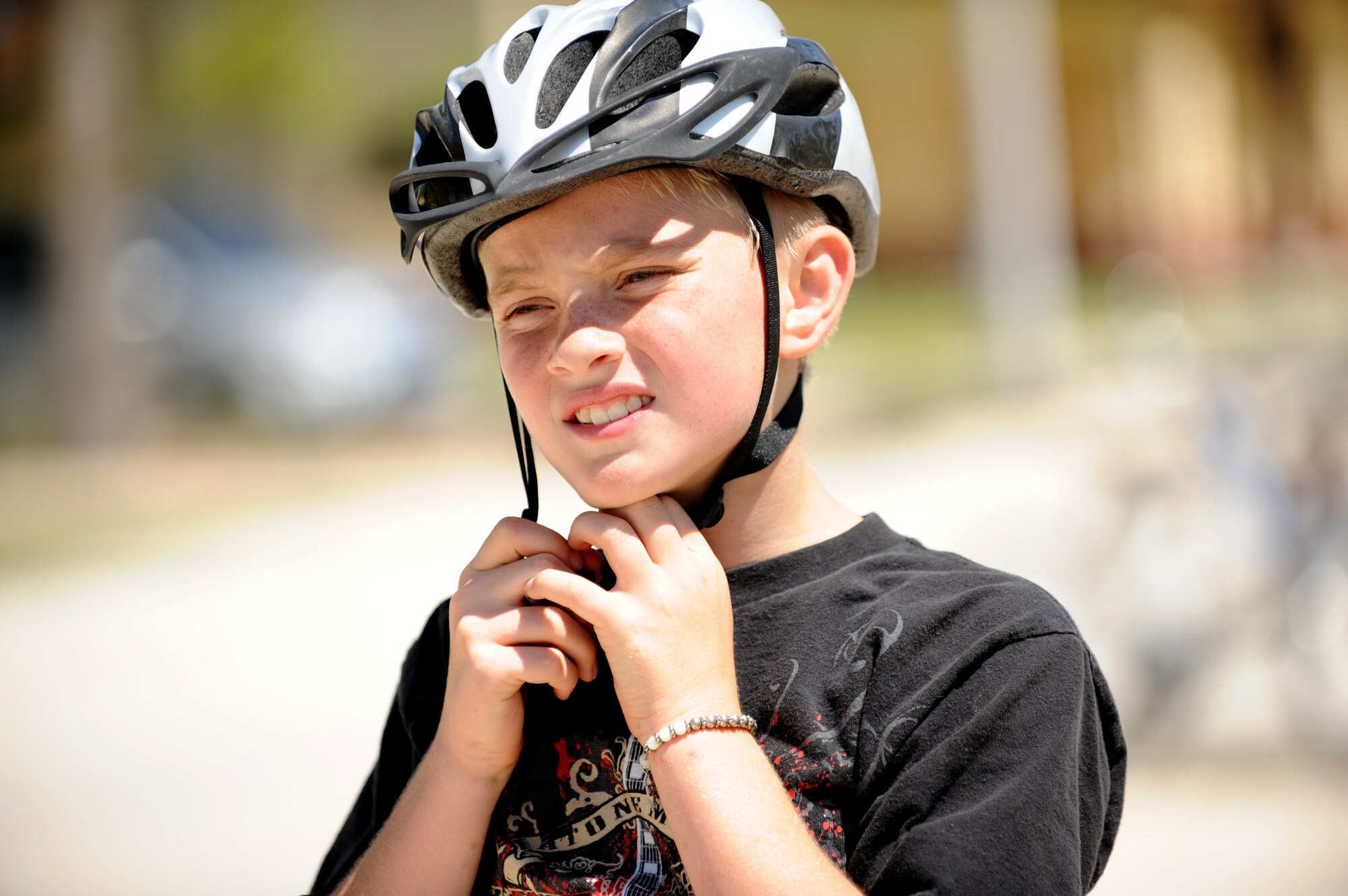 A boy secures his helmet during the Bicycle Safety Rodeo June 9, 2012, at Incirlik Air Base, Turkey. The annual event is designed to inform riders of all ages about proper safety techniques to use while riding a bicycle. (U.S. Air Force photo by Senior Airman Jarvie Z. Wallace/Released)