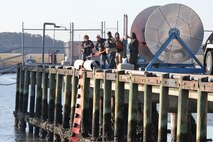 Members of the spill management team deploy a hard boom into the water at the Air Station fuel pier Nov. 2. The spill management team and facility response team work together to capture hazardous material in water. 