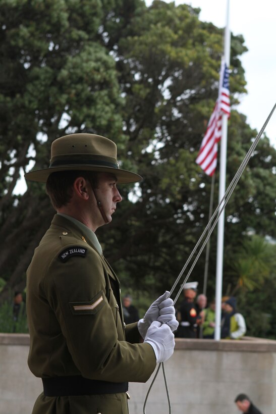 Lance Corporal Michael W. M. Dean, an engineer with 2nd Engineer Regiment, lowers the New Zealand colors in timing with the U.S. colors during a commemoration ceremony at the National War Memorial Here, here, June 14. Dean, a 26-year-old native of Oamaru, also stood guard at the foot of the memorial. Prominent government and military officials of the United States and New Zealand commemorated the 70th anniversary of the arrival of U.S. forces in Wellington during World War II. Australian and New Zealand forces were conducting heavy fighting in Northern Africa in 1942 while U.S. forces played a significant role in the defense of Oceania.::r::::n::(U.S. Marine Corps photo by Sgt. Jacob H. Harrer)::r::::n::