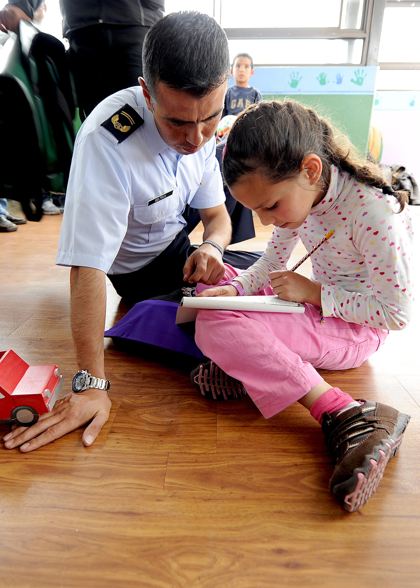A member of the Colombian air force spends time with a child from Asociación Amigos del Niño Ayudame, Bogota, Colombia how to put together a paper-model helicopter, as one of the donated items members of the Colombian air force and the 571st Mobility Support Advisory Squadron handed out during their visit to the orphanage June 9.  Airmen from both the Inter-American Air Forces Academy and 12th Air Force (Air Forces Southern) also participated in the visit.  (U.S. Air Force photo by Tech. Sgt. Lesley Waters)