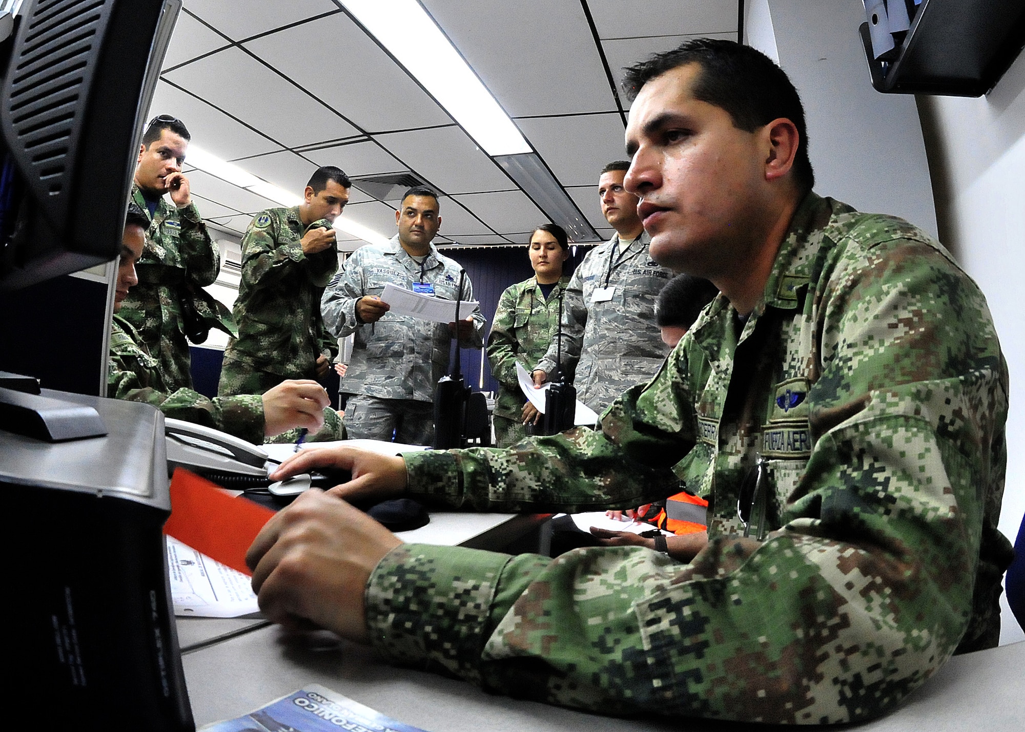 Master Sgt. Roberto Vasquez, 12th AF (AFSOUTH) heavy aircraft manager, and Technical Sgt. Melvin Rosario, Inter-American Air Forces Academy instructor, listen in as members of the Colombian air force maintenance operations centers go over the evening's flight schedule before the MOC briefing for senior leadership June 15, at Comando Aéreo de Combate No. 1 base, Palanquero, Colombia, as part of a month-long Air Mobility Command Building Partner Capacity mission. (U.S. Air Force photo by Tech. Sgt. Lesley Waters)