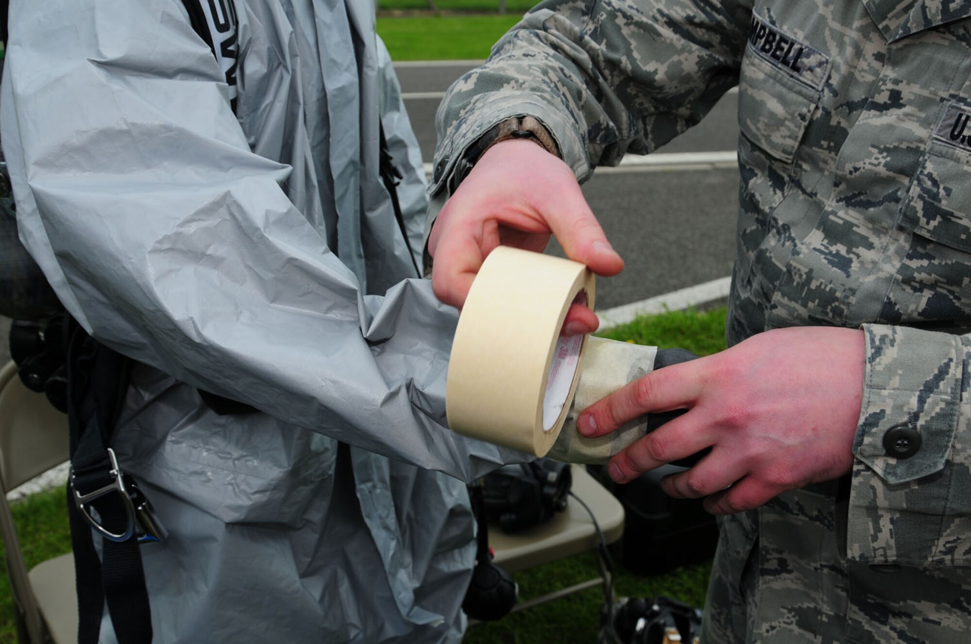 RAF MILDENHALL, England – Staff Sgt. Ian Campbell, right, 100th Civil Engineer Squadron Emergency Management, tapes the sleeves on the Level-B chemical protection suit worn by Airman 1st Class Joshua Foxworth, also 100th CES Emergency Management here June 12, 2012. The tape simulates chemical tape, which stops hazardous chemicals splashing onto and touching the skin. All openings get taped, including around cuffs and tops of boots, and around the respirator. Reservists from the 434th Civil Engineer Squadron, Grissom Air Reserve Base, Ind., have spent two weeks at RAF Mildenhall, working and training with the 100th CES. (U.S. Air Force photo/Karen Abeyasekere)
