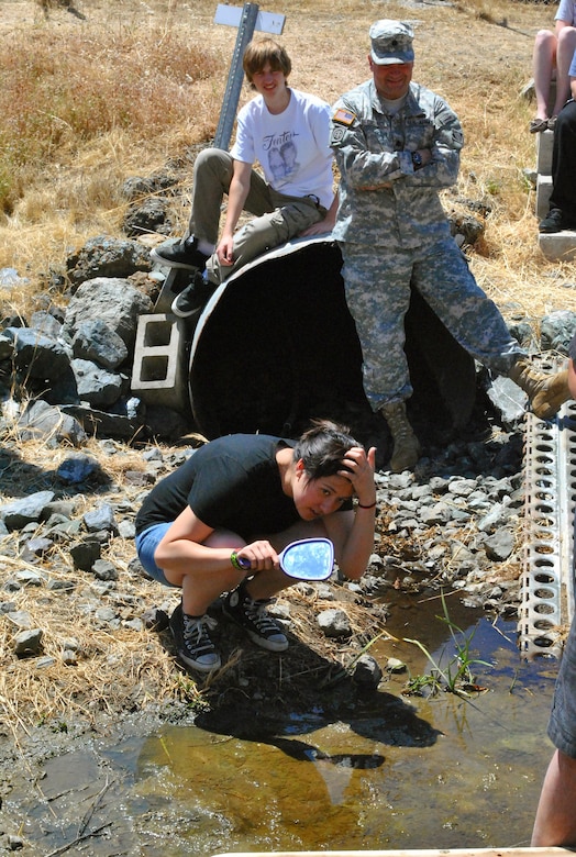 UKIAH, Calif. -- Stephanie Bond, a member of The Zombots, Vallejo High School's robotics team in California, searches for a robot in a large, narrow pipe along the Coyote Dam. The robot, developed by The Zombots, was brought to the dam to assess the interior conditions of the pipe. U.S. Army Corps of Engineers San Francisco District commander, Lt. Col. Torrey DiCiro and Zombots team member Jacob Holbrook look on.