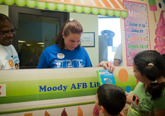 Erin Pearson, 23d Force Support Squadron head library clerk and storyteller, hands a book to a child in the library for the Summer Reading Program June 20, 2012, at Moody Air Force Base, Ga. Older children check out their own books and come in once a week to get their book log stamped, tracking how much they read. (U.S. Air Force photo by Airman 1st Class Jarrod Grammel/Released)
