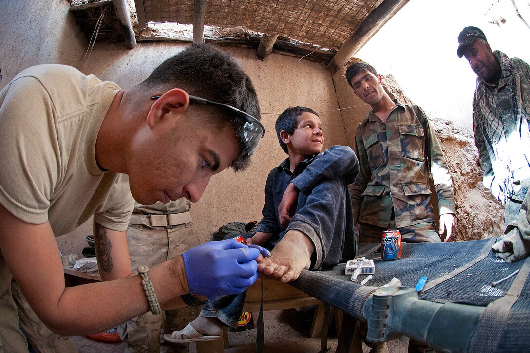 U.S. Army Pfc. Michael Trevino treats an injured toe of an Afghan boy who lives near Joint Security Station Hasan in the Gilan district in southern Afghanistan's Ghazni province, June 13, 2012. Trevino, a medic, is assigned to the 82nd Airborne Division's 1st Battalion, 504th Parachute Infantry Regiment, 1st Brigade Combat Team.
