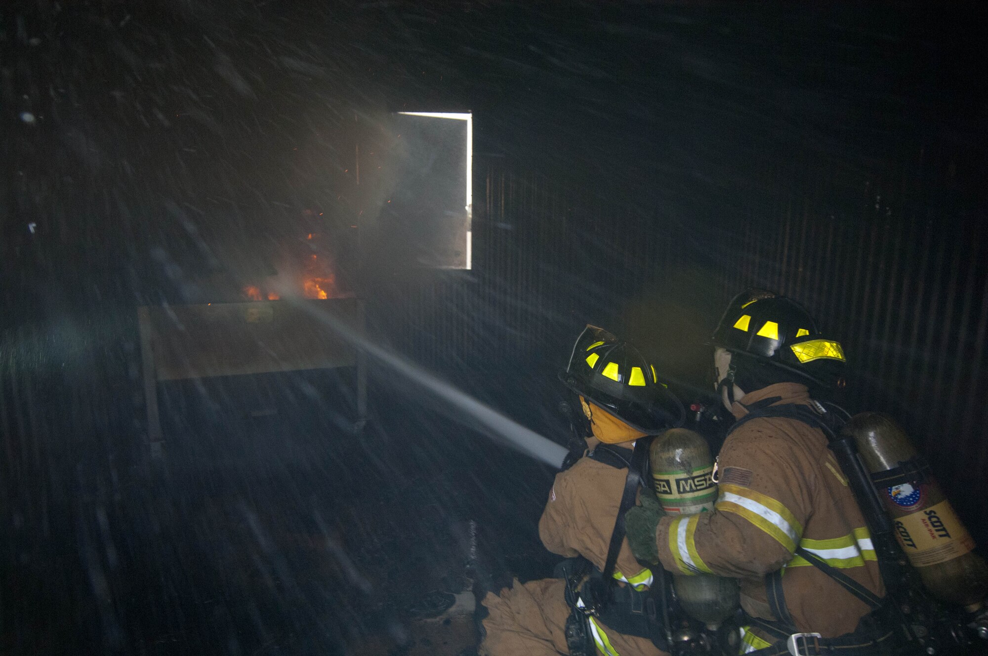 Airman 1st Class James Blair, and Bill Cina, 28th Civil Engineer Squadron fire protection specialists, extinguish flames in a controlled exercise at the structural burn training facility at Ellsworth Air Force Base, S.D., June 18, 2012. The 28th CES fire department routinely conducts various training scenarios to maintain mission readiness. (U.S. Air Force photo by Airman 1st Class Zachary Hada/Released)