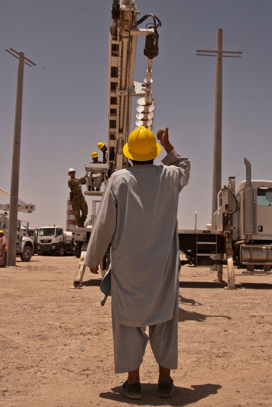 KANDAHAR AIRFIELD, Afghanistan — An Afghan electrical technicians practice hand signals while a fellow student learns how to operate a truck-mounted augur system used to emplace utility poles during a 10-day class led by the U.S. Army Corps of Engineers South District's non commissioned officers, June 10-19 2012.