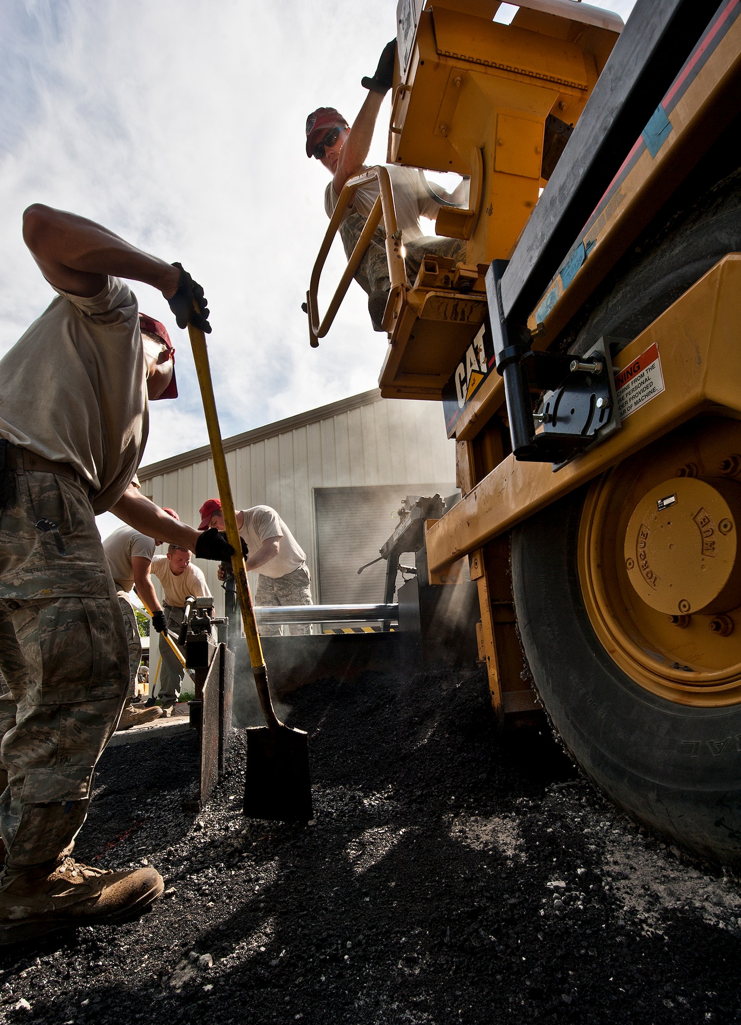 The Red Hats of the 823rd Red Horse Squadron spread out the asphalt that the paver puts down at the Combat Shield compound at Eglin Air Force Base, Fla., June 20.  The two-month paving project by the Hulburt Field Airmen changed the layout of the roads in and out of the compound to allow for large haulers to maneuver and exit with ease.  (U.S. Air Force photo/Samuel King Jr.)