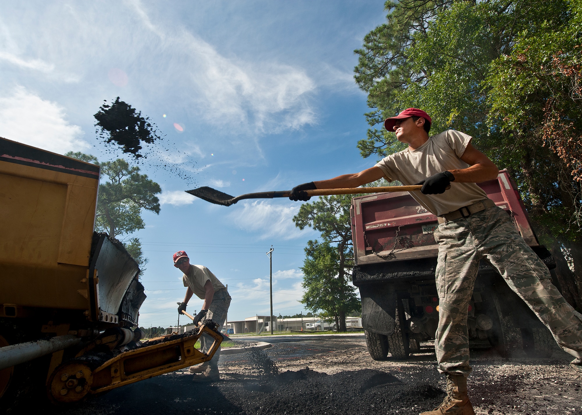 Airman 1st Class Anthony Abreu, of the 823rd Red Horse Squadron, tosses a shovel-full of asphalt back into the paver June 20 at Eglin Air Force Base, Fla.  The two-month paving project of the Combat Shield compound was a redesign of the roads in and out of the compound to allow for large haulers to maneuver and exit with ease.  Most of the planning and all of the labor were performed by Red Horse Airmen.  (U.S. Air Force photo/Samuel King Jr.)