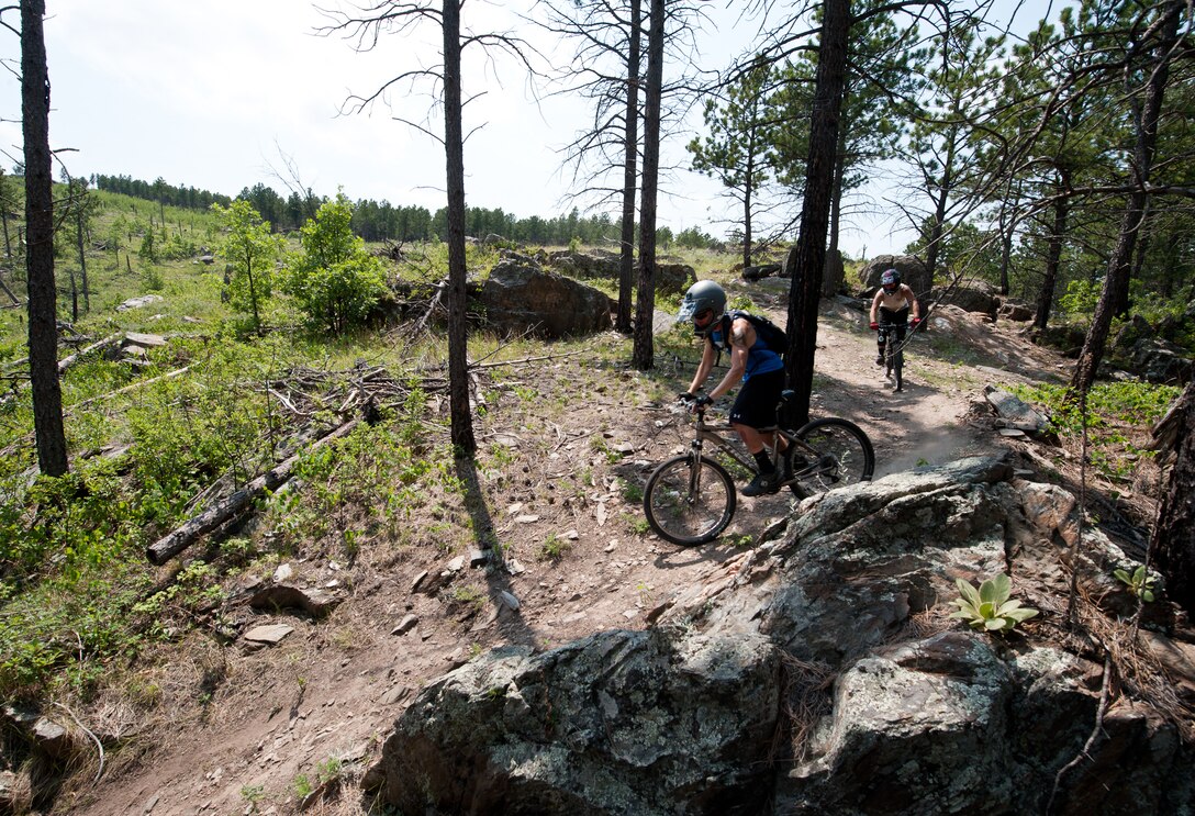 Airman 1st Class Brody Schneider, (left) and Senior Airman Justin Faircloth, 28th Operations Support Squadron air traffic control technicians, weave around rocks while mountain biking down Storm Mountain, S.D., June 24, 2012. The 28th Force Support Squadron Outdoor Recreation Center has bicycles and safety equipment available for rent. For more information, call the Outdoor Recreation Center off at (605) 385-2999. (U.S. Air Force photo by Airman 1st Class Alystria Maurer/Released)