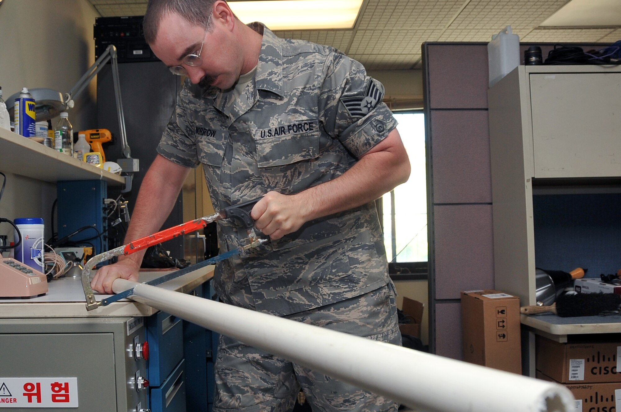 Staff Sgt. Lucas Morrow, American Forces Network broadcaster, saws PVC pipe to make a make a smaller version of a modified camera stabilizing mount at Osan Air Base, Republic of Korea, June 27, 2012. Morrow’s original design needed the camera man to wear a vest. This product will eliminate the vest, and be placed upon the shoulders. (U.S. Air Force photo/Staff Sgt. Craig Cisek) 